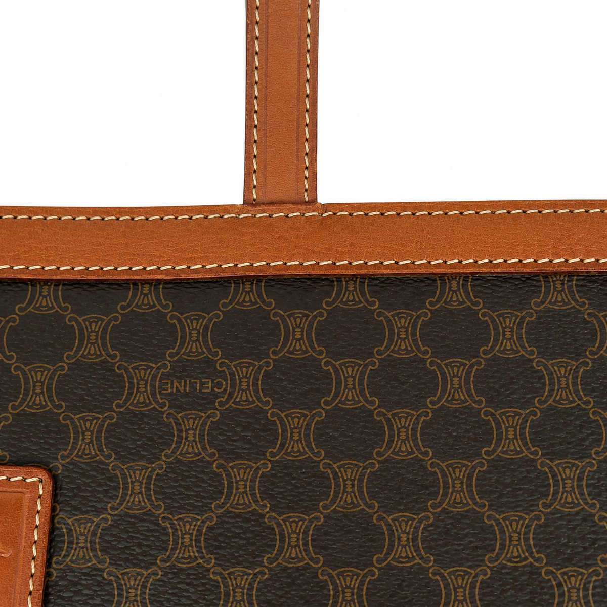 Close-up of a Celine monogrammed bag featuring dark brown coated canvas with a tan repeating logo pattern, tan leather trim with white stitching, and a small embossed Celine logo.