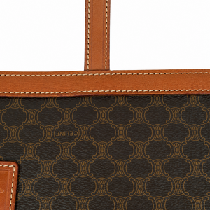 Close-up of a Celine monogrammed bag featuring dark brown coated canvas with a tan repeating logo pattern, tan leather trim with white stitching, and a small embossed Celine logo.