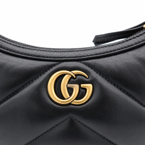 Close-up of a black quilted leather handbag featuring a prominent gold-tone interlocking GG logo on the front, set against a clean white background.
