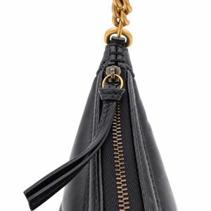 Close-up detail of a black leather handbag showing a black zipper with a leather pull tab, gold-tone hardware ring, and a gold chain attachment against a white background.