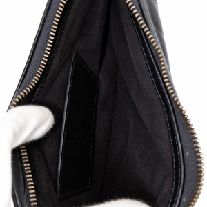 Close-up of the interior of a black leather bag with a black fabric lining, gold-toned zipper, and a white-gloved hand holding it open against a white background.