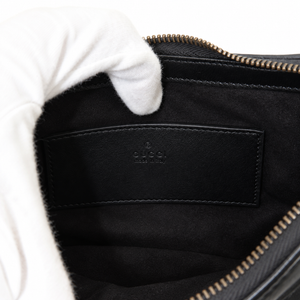 Close-up of a black Gucci pouch or bag interior with a white-gloved hand holding it open, showing the black suede-like interior lining and embossed Gucci logo patch.