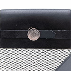 A close-up of a black leather Hermès Paris card holder or wallet with a silver-tone circular logo clasp and a black leather strap across the front, set against a white mesh background.