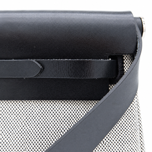 Close-up detail of a black leather bag with a textured black-and-white woven fabric body and a matching black strap on a white background.