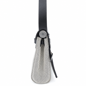 A close-up side view of a handbag showing a textured silver mesh body, a black leather strap, and a circular silver-tone metal clasp on a plain white background.