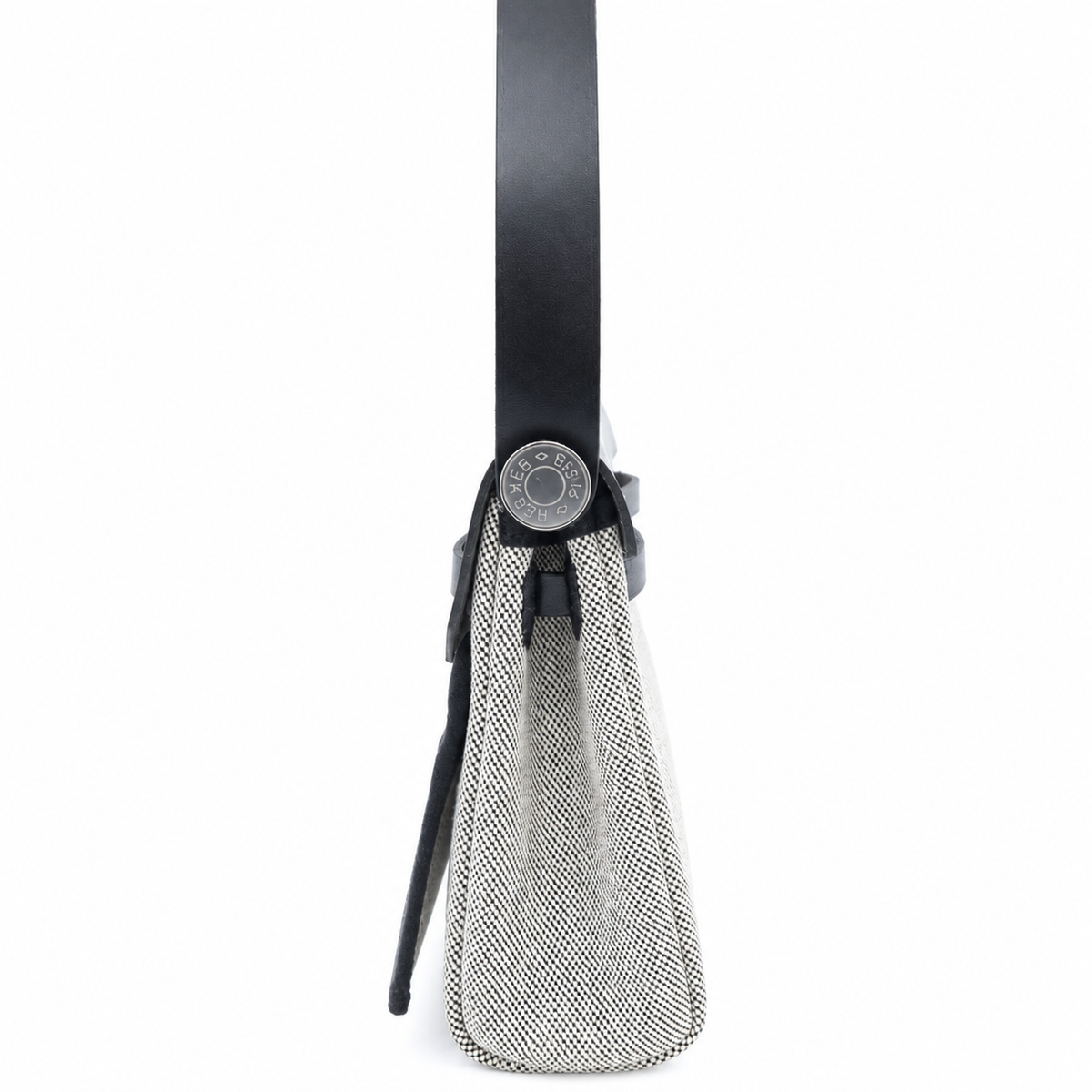 A close-up side view of a handbag showing its black leather strap, black hardware, and a textured black and white woven fabric body, set against a plain white background.
