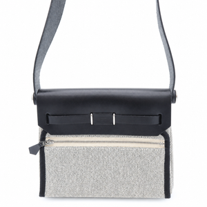 A structured crossbody bag with a black leather flap and shoulder strap, paired with a textured light gray woven front panel and a zippered pocket.