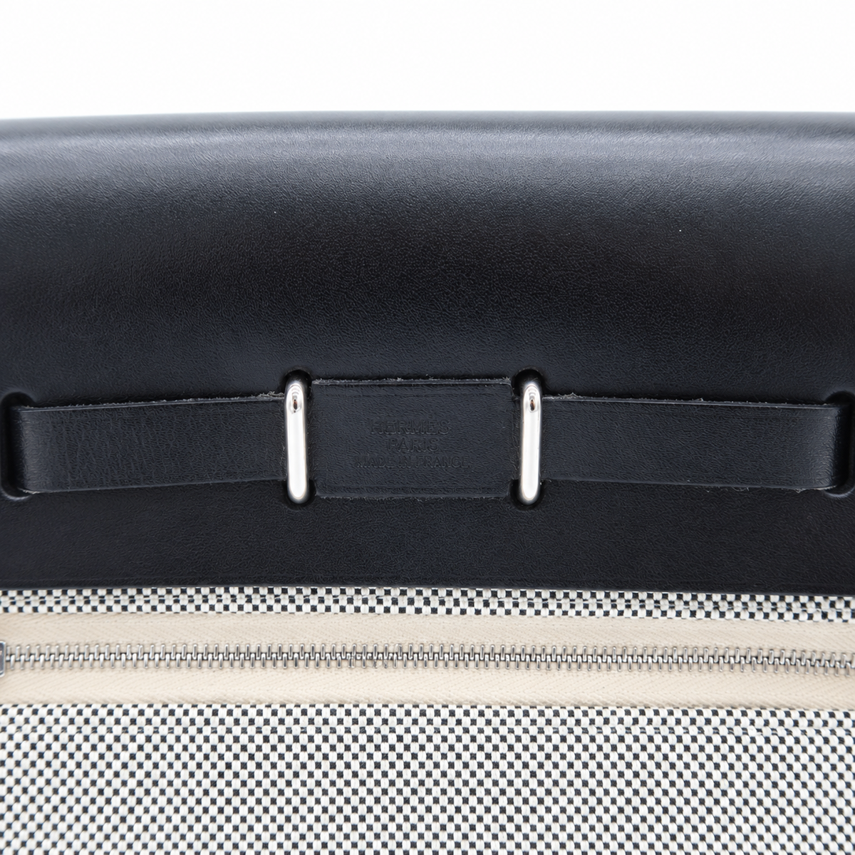 Close-up of a black leather strap with silver metal rivets and a silver zipper on a white mesh fabric surface.
