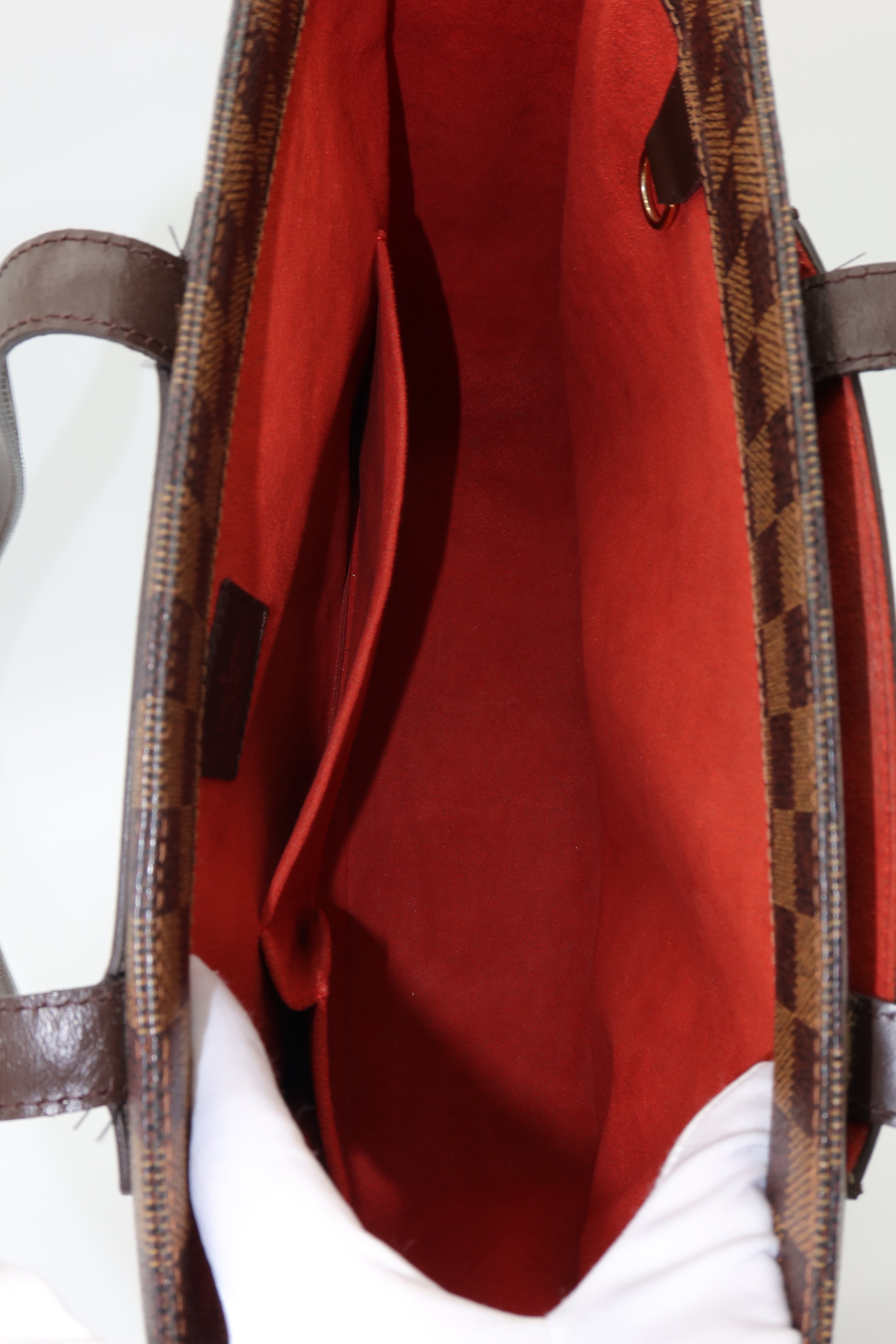 Close-up of the interior of a handbag, showing a red fabric lining and a brown patterned exterior edge with dark brown handles.