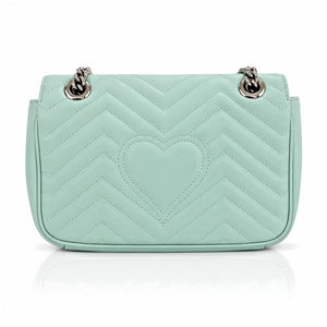 A mint green quilted leather shoulder bag with a central heart motif and silver-tone chain strap hardware, shown against a plain white background with a soft reflection below.