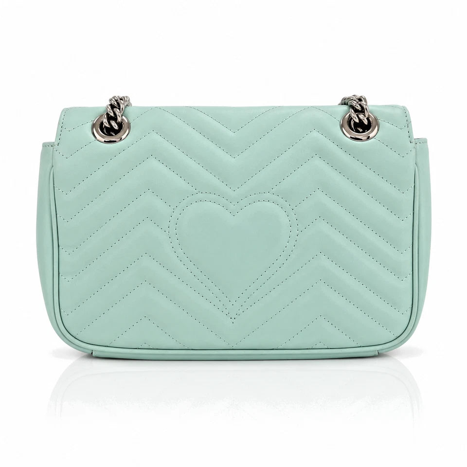 A mint green quilted leather shoulder bag with a central heart motif and silver-tone chain strap hardware, shown against a plain white background with a soft reflection below.