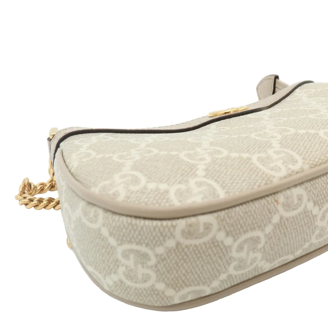 A close-up of a beige and off-white monogram handbag with a gold chain strap, shown on a clean white background.