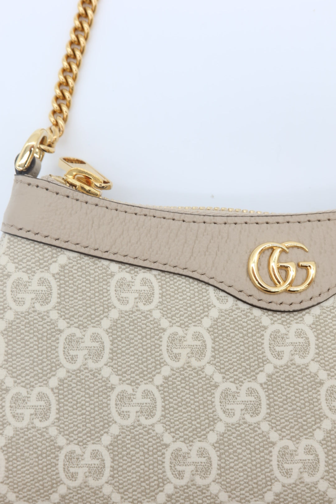 Close-up of a Gucci shoulder bag featuring beige GG Supreme canvas, a beige leather trim, and a gold-tone chain strap with a gold interlocking GG logo.