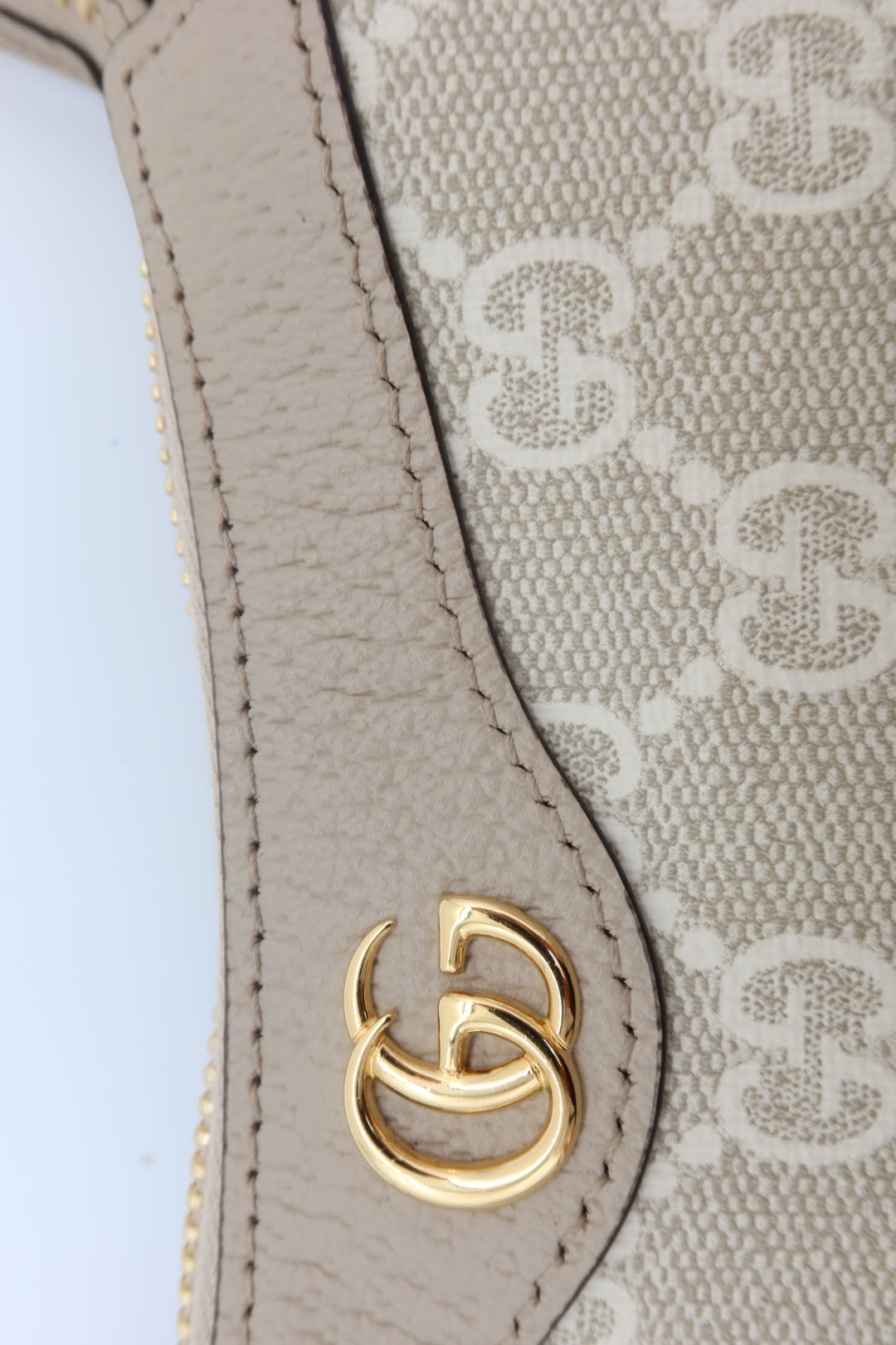 Close-up of a Gucci handbag featuring beige and off-white GG Supreme canvas with a beige leather trim and a gold-tone interlocking GG logo clasp.