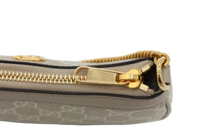 Close-up of a beige and brown monogram clutch or pouch with a gold zipper and gold hardware, featuring the Gucci logo pattern and a gold zipper pull engraved with 'GUCCI'.