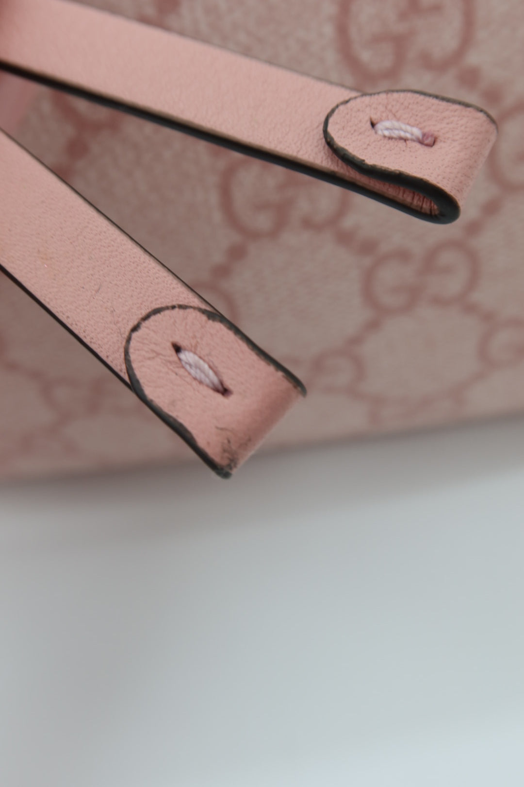 Close-up detail of a light pink leather strap with black edging and a matching pink monogram patterned background.
