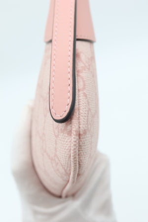 A close-up of a light pink textured handbag with a matching pink leather strap and black trim, held by a white-gloved hand against a white background.