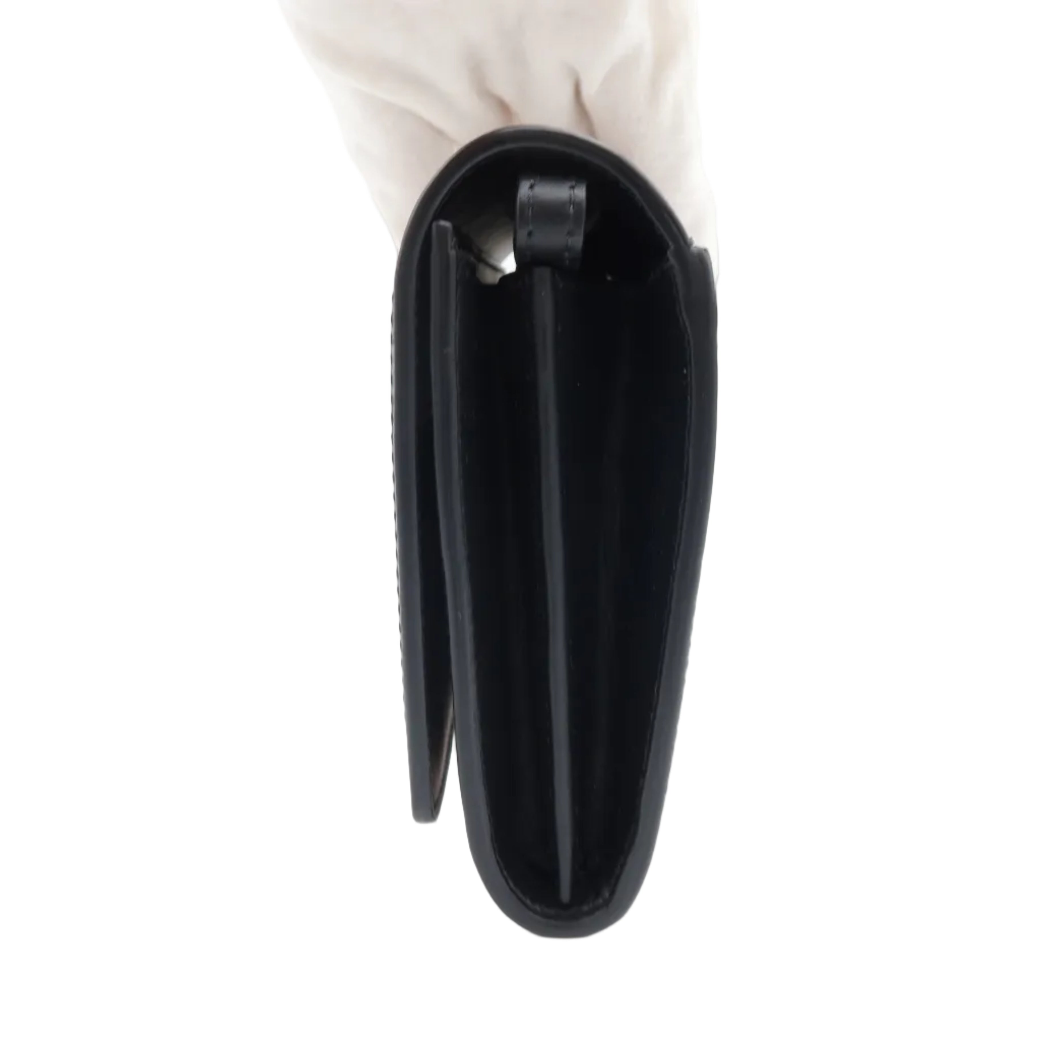 A black leather clutch or wallet-style handbag shown closed from the side, held by a white gloved hand against a plain white background.