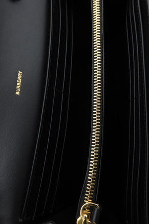Close-up of a black leather wallet or clutch with multiple vertical card slots, a gold zipper, and a small gold BURBERRY logo on the left side.