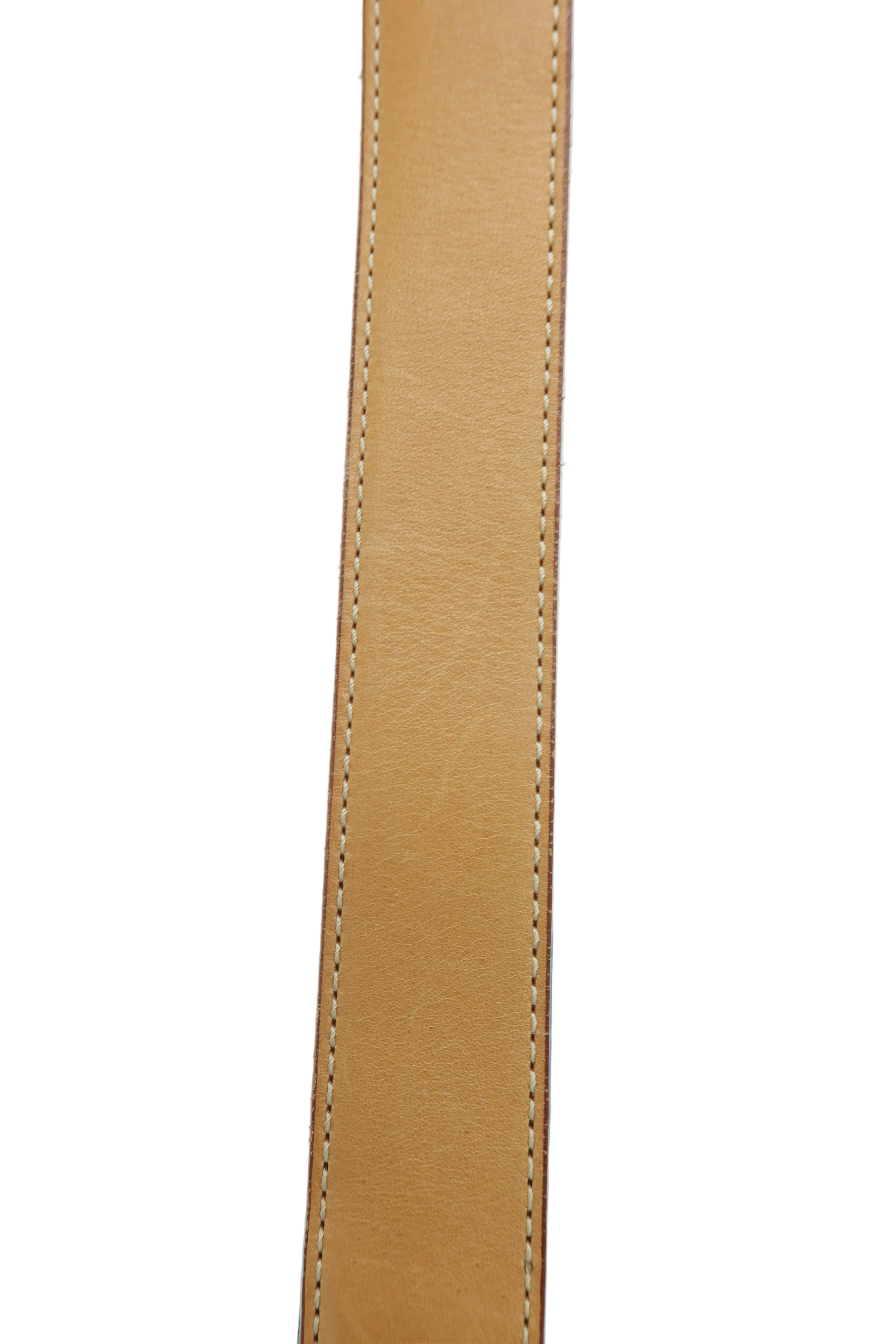 Close-up of a tan leather strap with neat contrast stitching, positioned vertically against a light blue background.