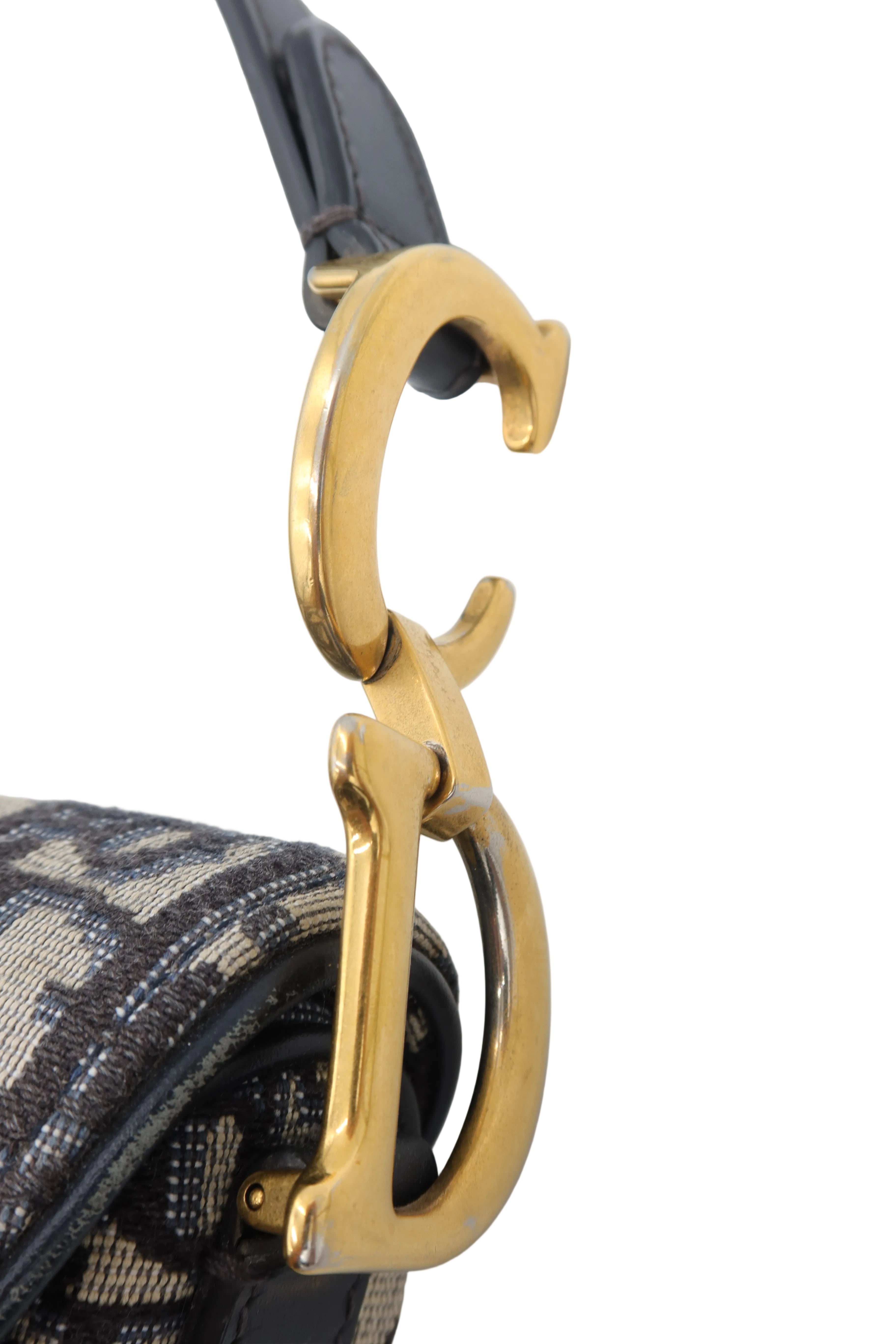 Close-up of a designer handbag featuring a polished gold-tone interlocking 'CD' clasp on a black leather strap, attached to a black and gold monogram canvas body.