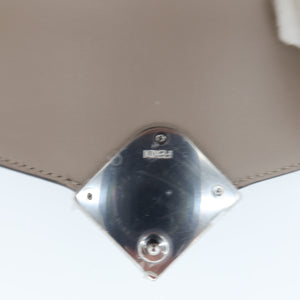 Close-up of a beige leather handbag showing the underside of the flap and a shiny silver-tone metal clasp with the brand name 'MINKA' visible.