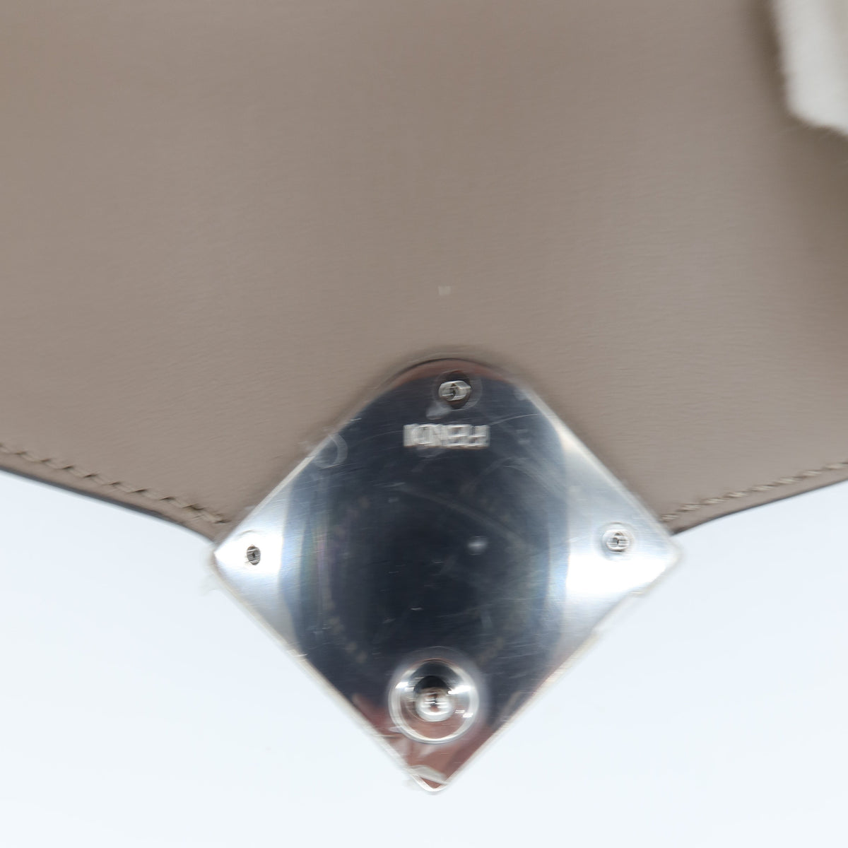 Close-up of a beige leather handbag showing the underside of the flap and a shiny silver-tone metal clasp with the brand name 'MINKA' visible.