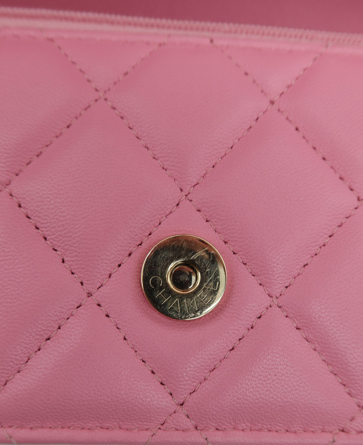 A close-up of a pink quilted leather clutch or wallet featuring a gold-tone circular snap button engraved with the brand name CHANEL.