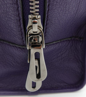 Close-up of a purple textured leather zipper pull with a silver-tone metal slider and a small embossed brand mark on the pull tab.