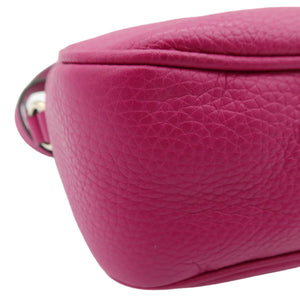 A close-up of a bright pink pebbled leather bag corner showing the texture and a small portion of the strap with a silver metal ring, on a white background.