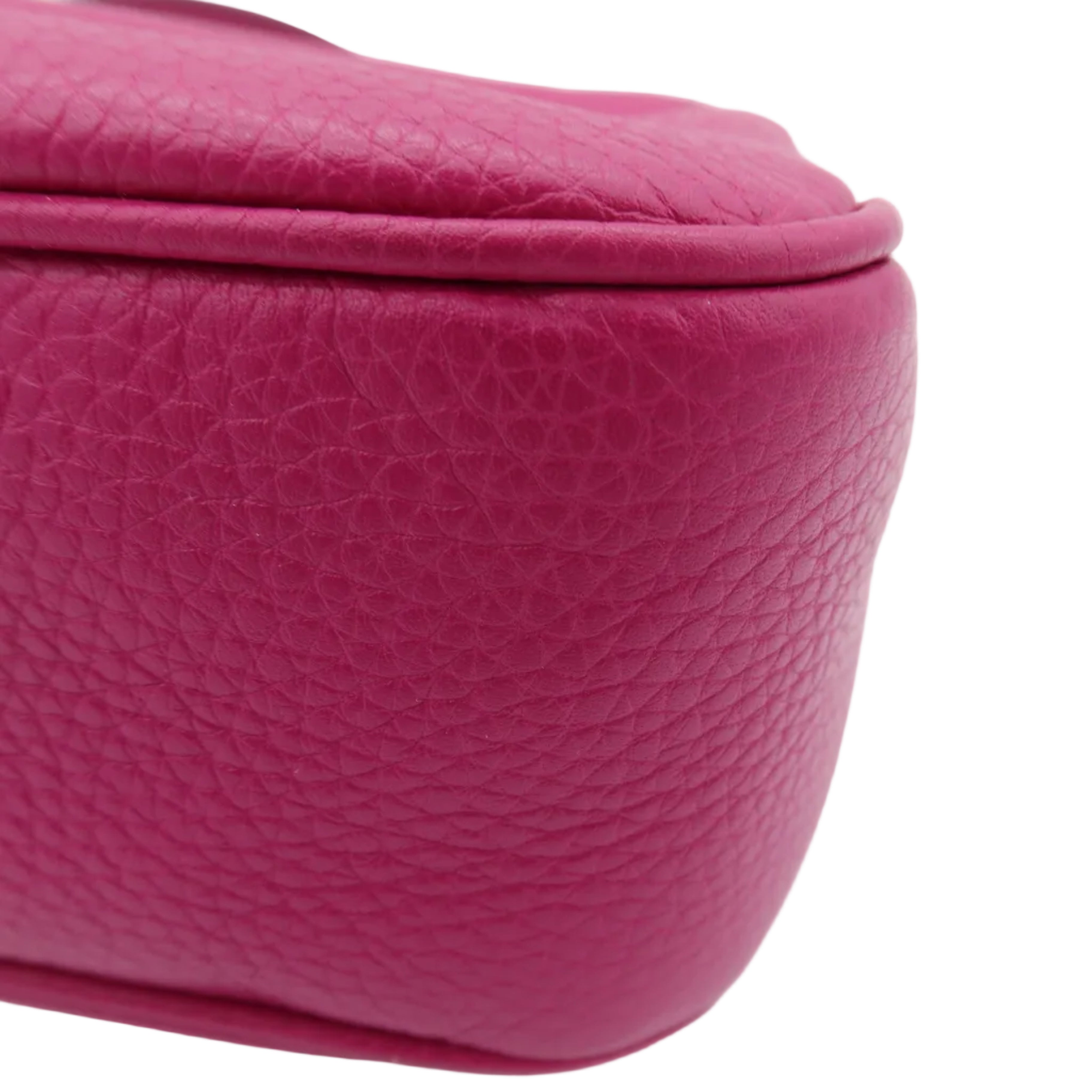 A close-up shot of a vibrant magenta pebbled leather bag corner on a clean white background.