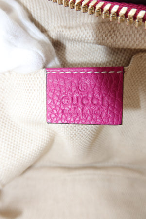 Close-up of a Gucci leather interior label in bright pink textured leather, stitched onto a beige woven fabric surface with a striped zipper visible at the top.