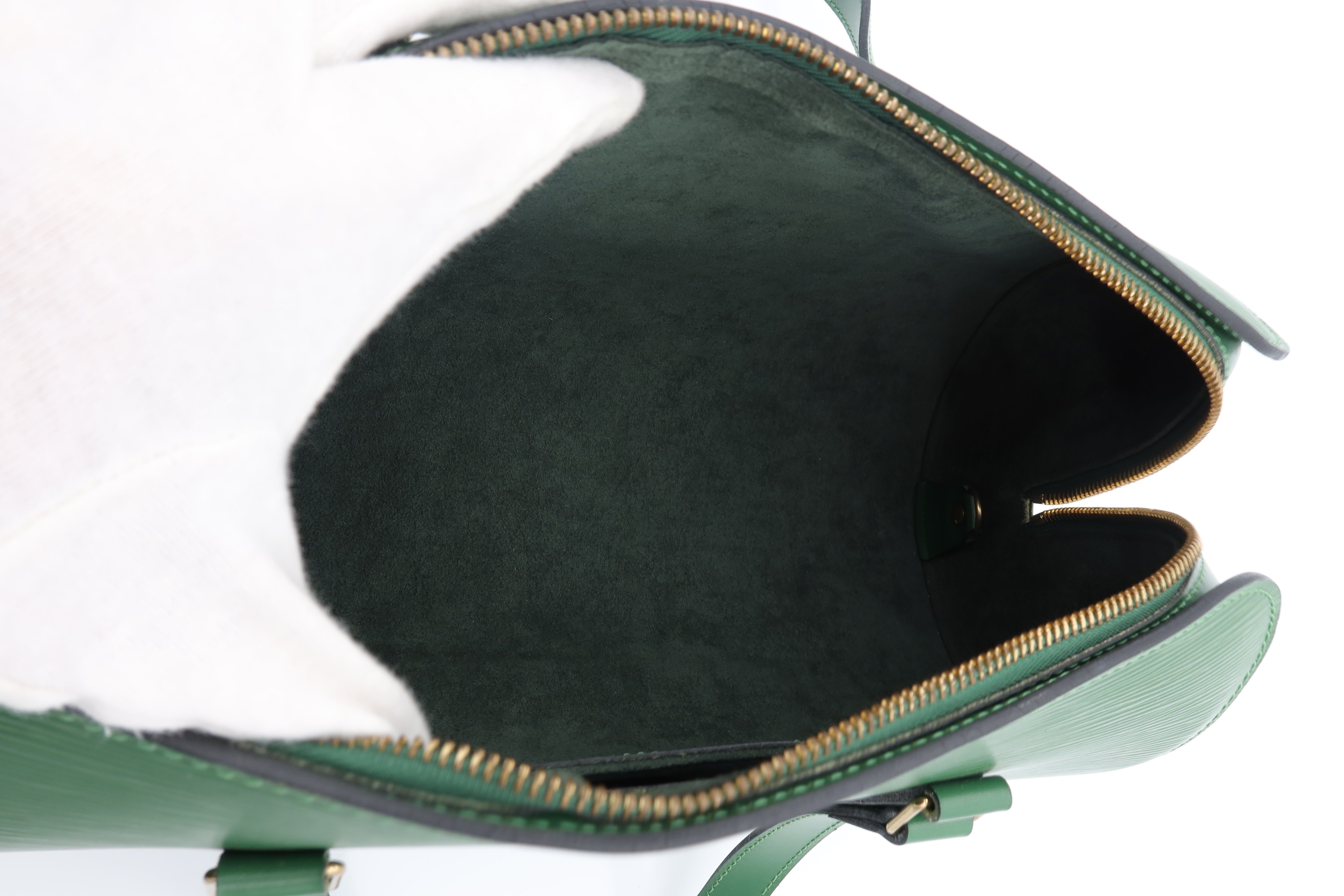 Close-up of the interior of a green leather handbag, showing a dark green suede-like lining and a gold-tone zipper.