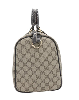 A small Gucci handbag in beige and brown GG Supreme canvas with dark brown leather trim, dual top handles, and gold-tone hardware, photographed against a plain white background.