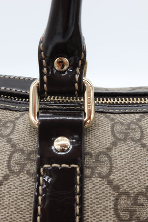 Close-up of a Gucci handbag featuring the brand's signature GG monogram canvas in beige and brown, a glossy black patent leather strap, and gold-tone hardware.