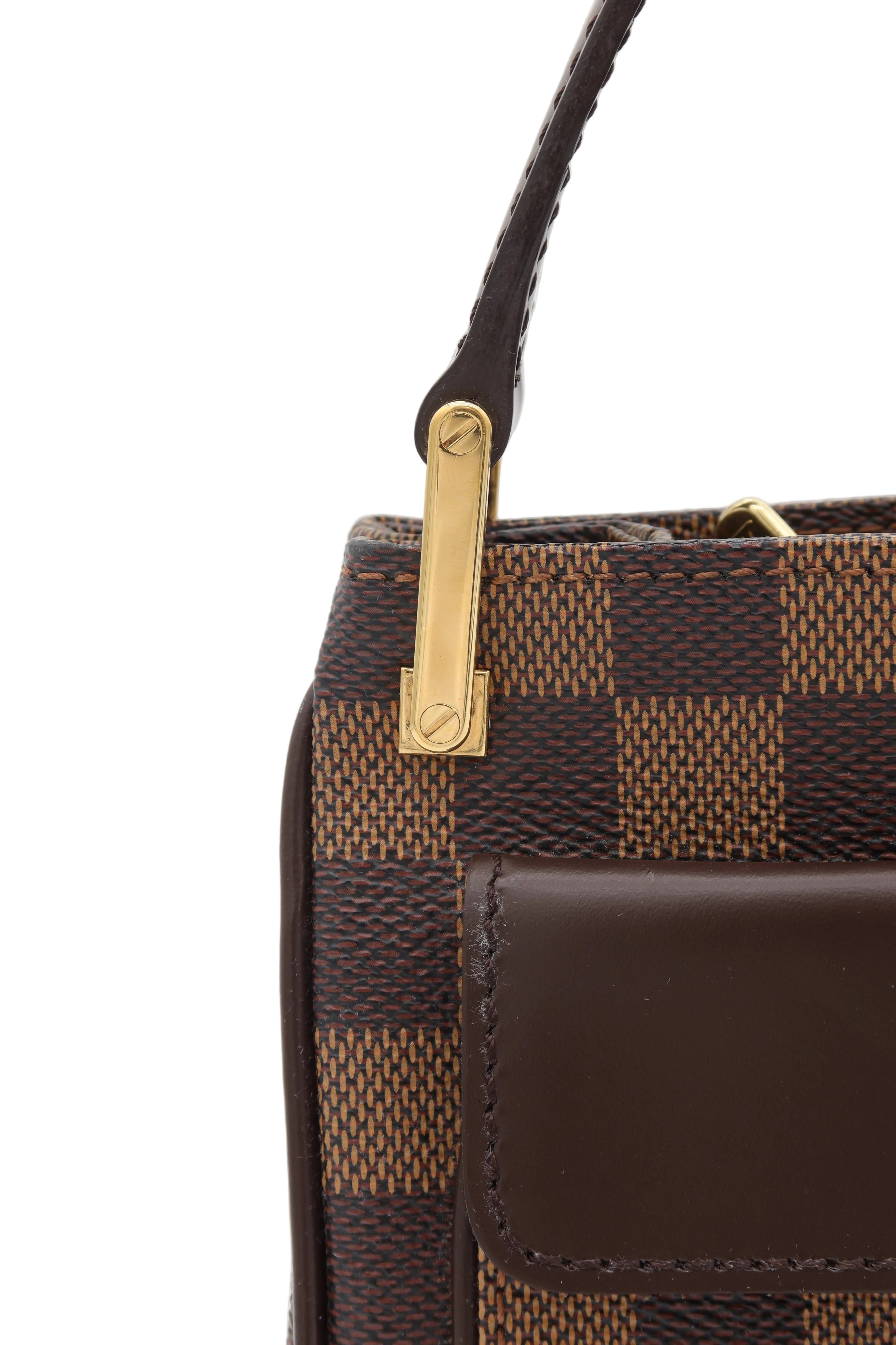 Close-up of a brown checkered handbag with a dark brown leather handle and a gold-tone metal clasp on a light gray background.