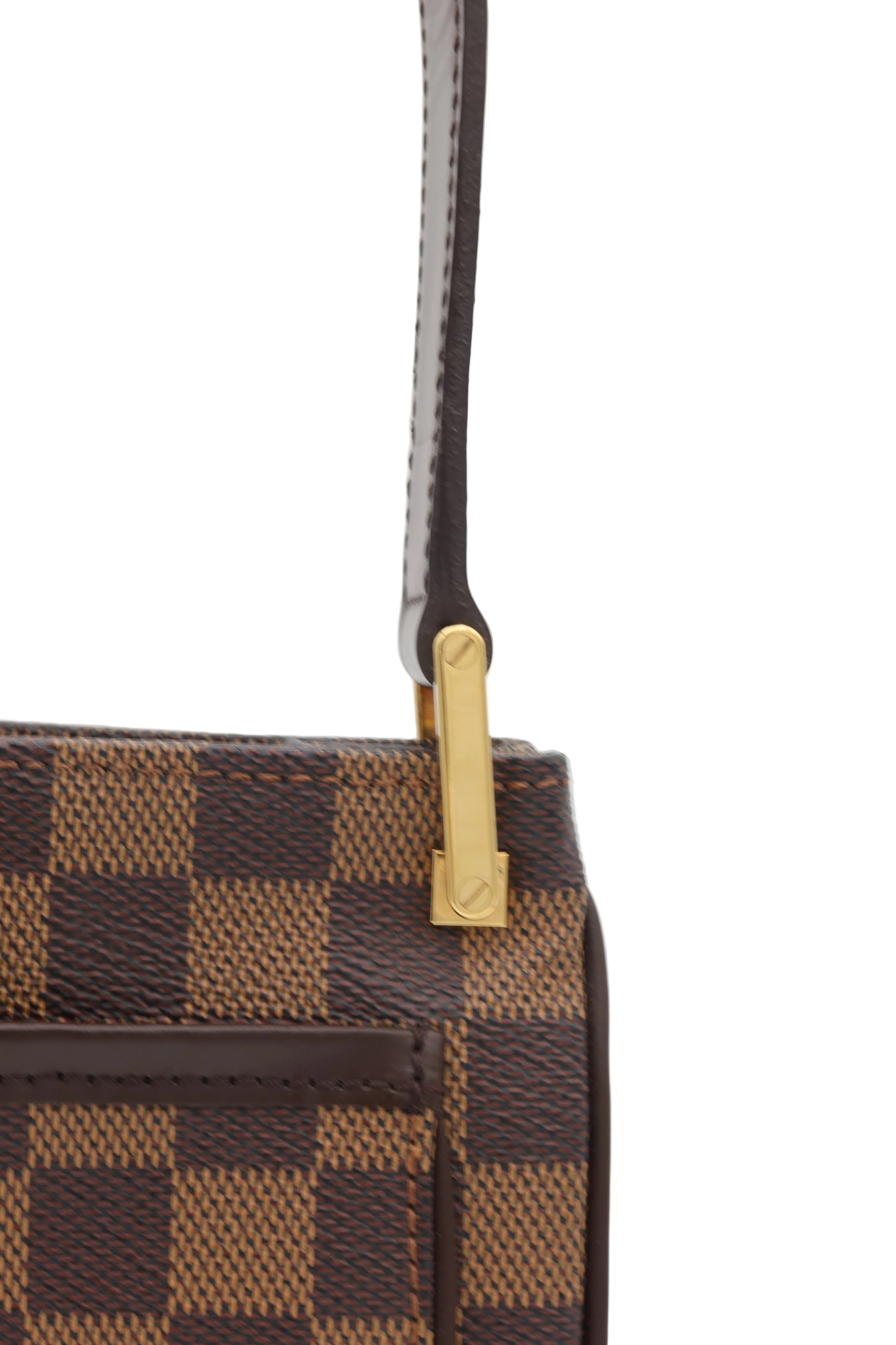 Close-up of a Louis Vuitton handbag in the Damier Ebene checkered canvas, featuring a brown leather strap with a gold-tone metal hardware clasp on a light gray background.