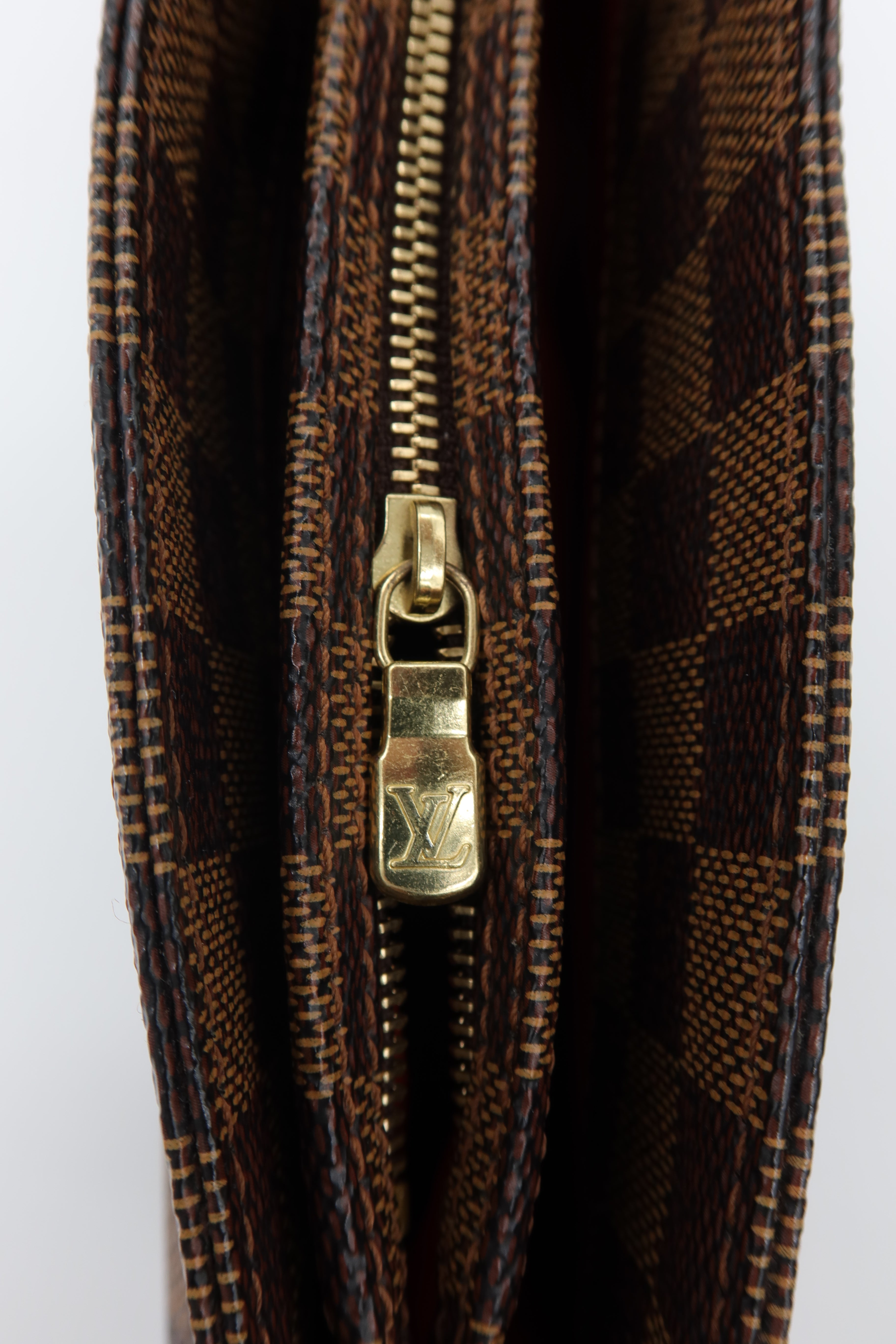 Close-up of a Louis Vuitton monogram canvas zipper, showing the classic brown and black check pattern with a gold-tone metal zipper pull engraved with the LV logo.