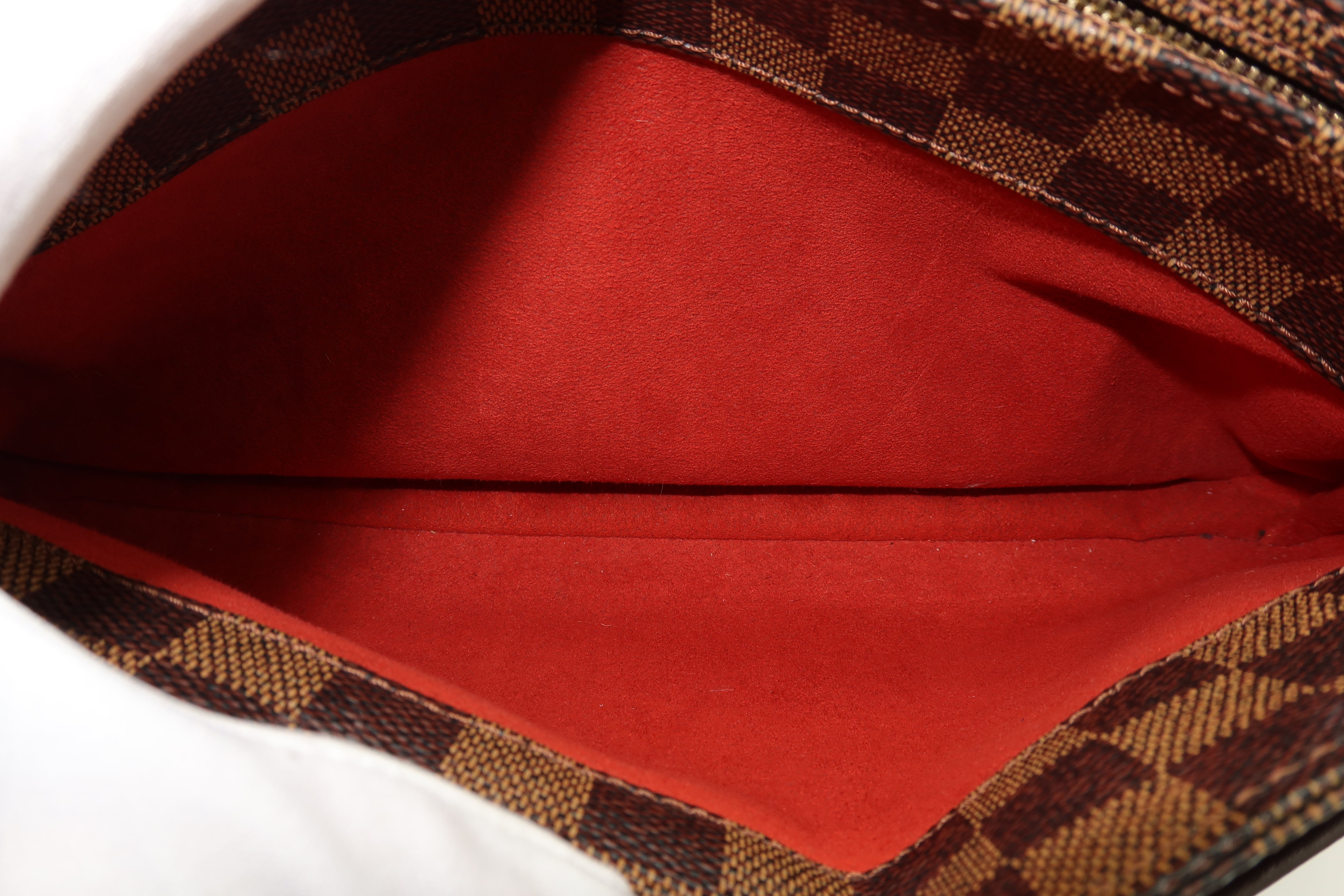 Close-up of the interior of a handbag or pouch, showing a bright red suede-like lining and a brown and beige checkered patterned fabric edge.