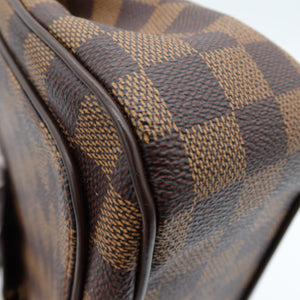 Close-up of a brown and tan checkered canvas bag corner with dark brown trim, showing the textured pattern and edge detail against a light background.