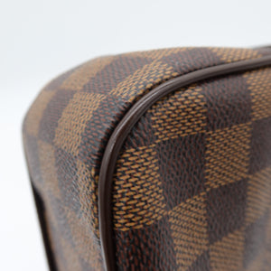 Close-up of a Louis Vuitton Damier canvas bag corner showing the brown and tan checkered pattern and dark brown leather trim against a white background.