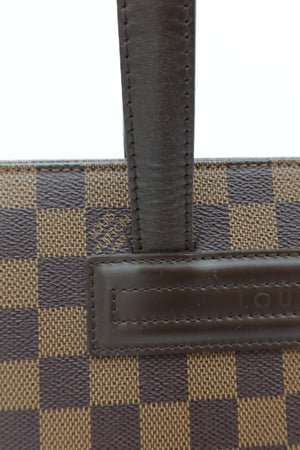 Close-up of a Louis Vuitton handbag featuring the brand's Damier check pattern in brown and beige canvas, with a dark brown leather strap and a leather patch embossed with the Louis Vuitton name.