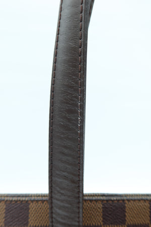 Close-up of a dark brown leather handle with visible stitching, set against a light blue background and a brown checkered fabric edge at the bottom.