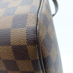 Close-up of a brown and tan checkered coated canvas bag surface with dark brown leather trim and a strap against a white background.