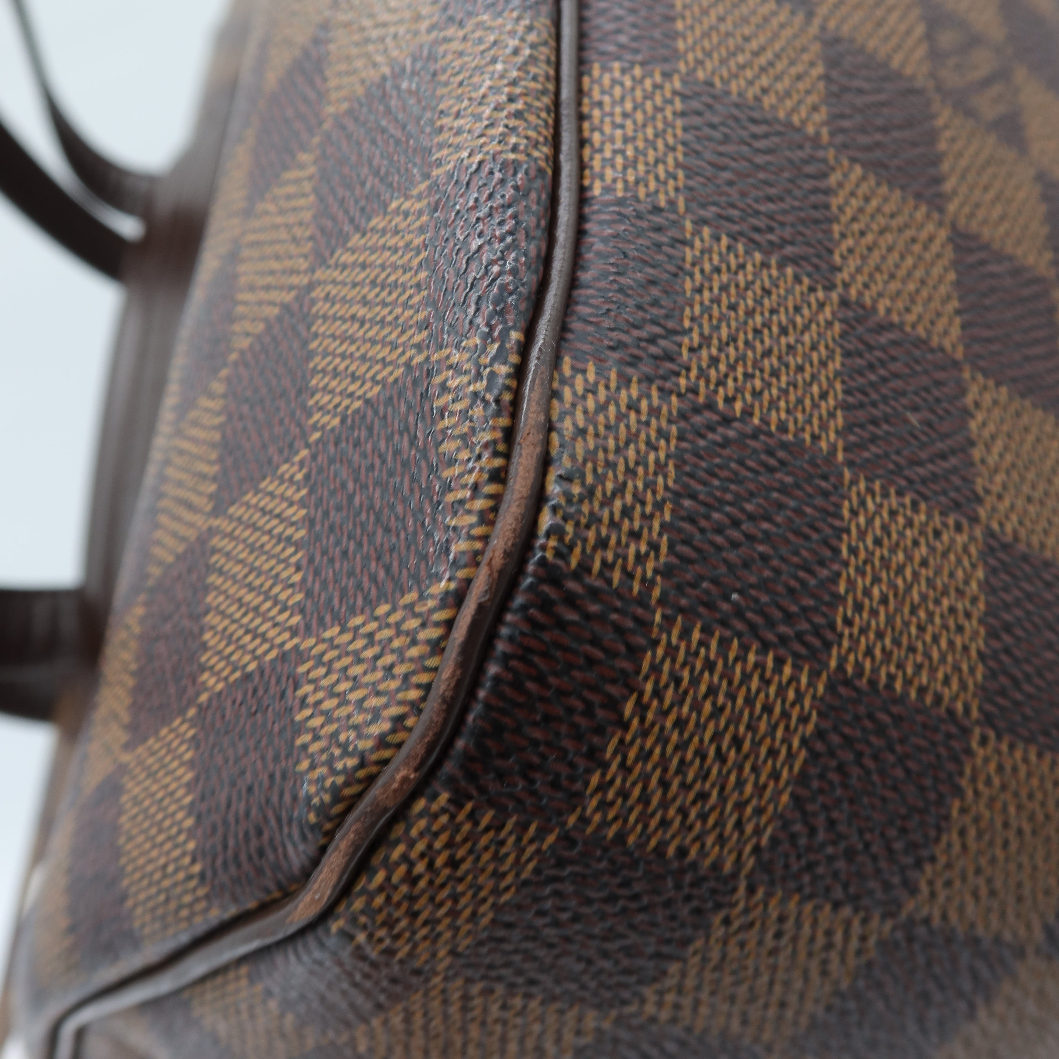 Close-up of a Louis Vuitton handbag in Damier Ebene canvas, showing the classic brown and beige checkered pattern and dark brown leather trim.