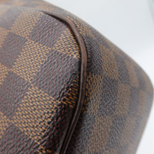 Close-up of a brown and tan checkered coated canvas surface with a dark brown leather edge, showing the texture and pattern detail.