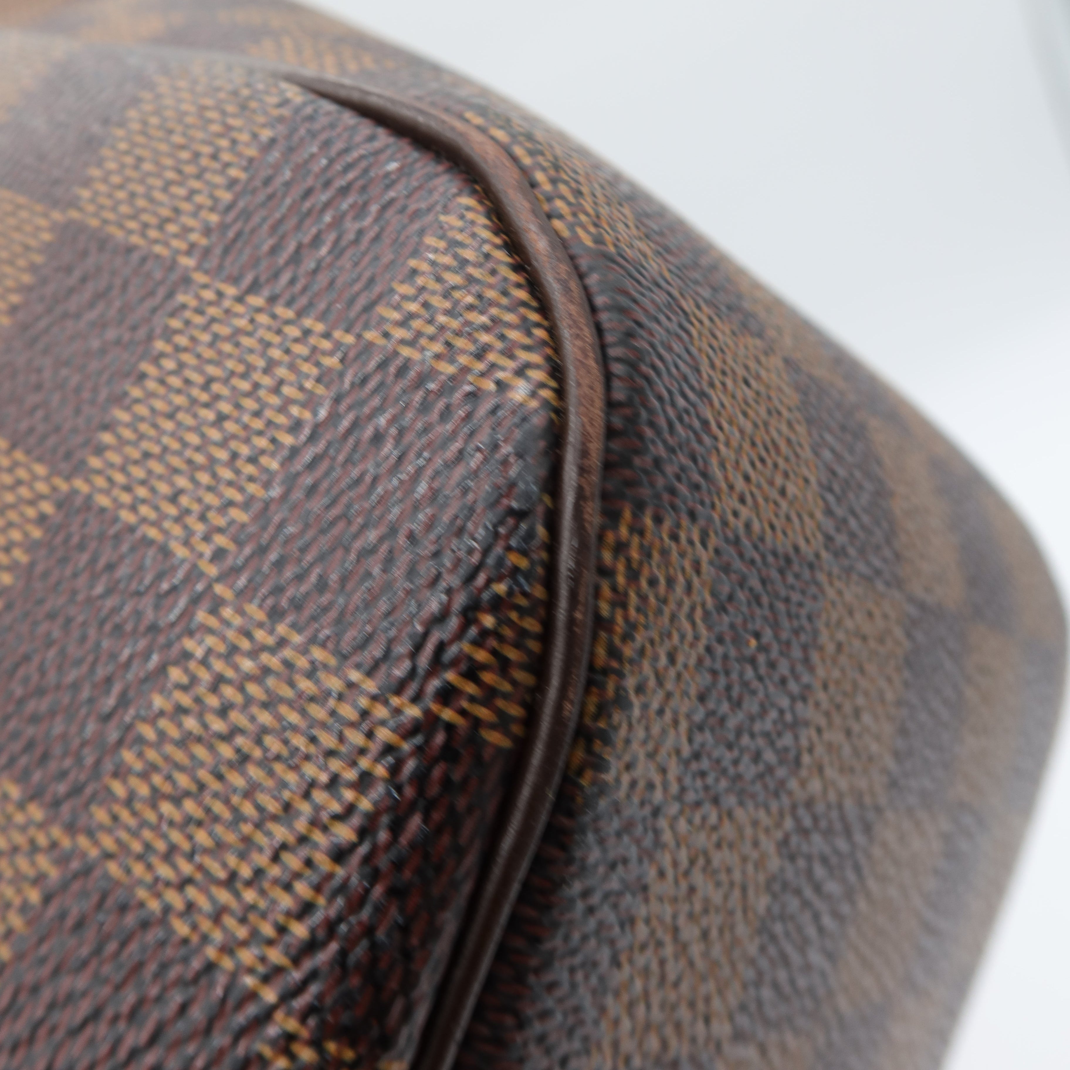 Close-up of a brown and tan checkered coated canvas surface with a dark brown leather edge, showing the texture and pattern detail.