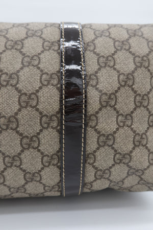 Close-up of a cylindrical product featuring beige and brown GG Supreme canvas with a glossy black leather band running vertically down the center.