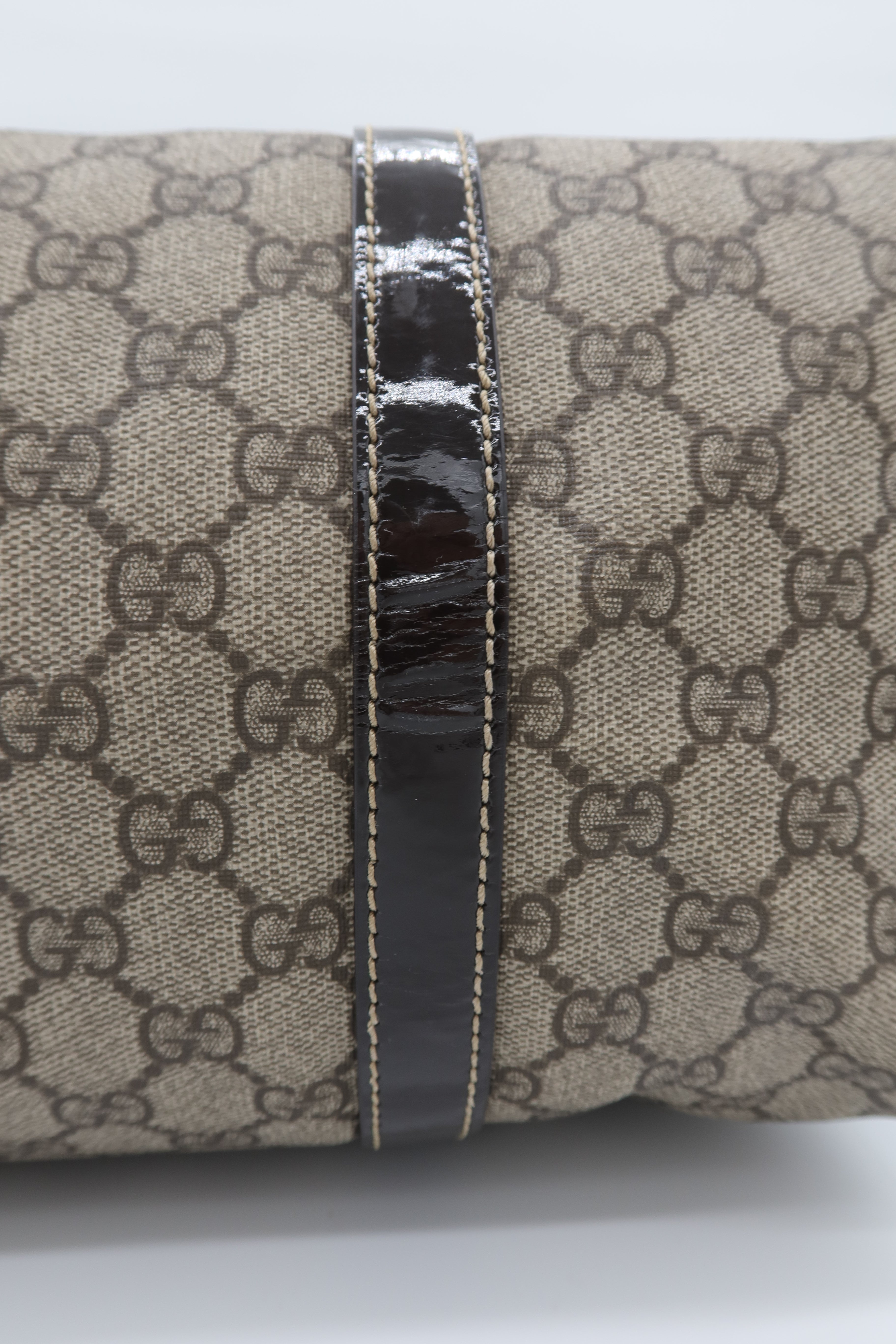 Close-up of a cylindrical product featuring beige and brown GG Supreme canvas with a glossy black leather band running vertically down the center.