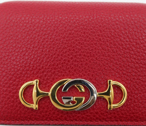 A close-up of a red pebbled leather wallet or clutch featuring a gold-tone and silver-tone interlocking G logo clasp, identified as Gucci.